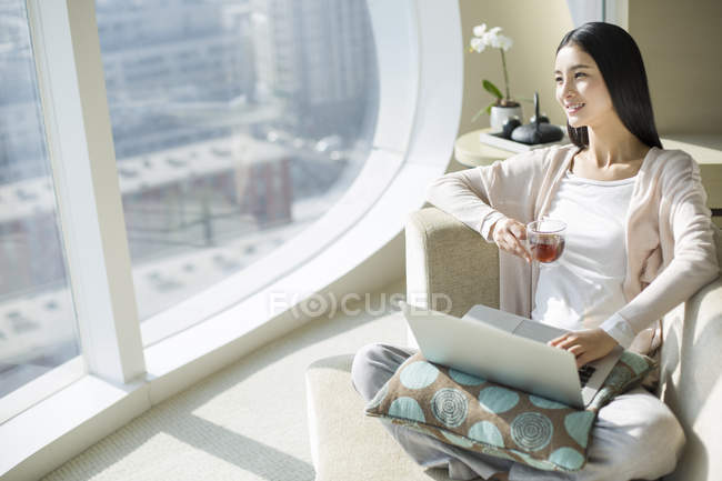 Chinês mulher bebendo chá no sofá com laptop — Fotografia de Stock