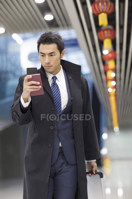 Hombre de negocios chino caminando en el aeropuerto con pasaporte y smartphone - foto de stock
