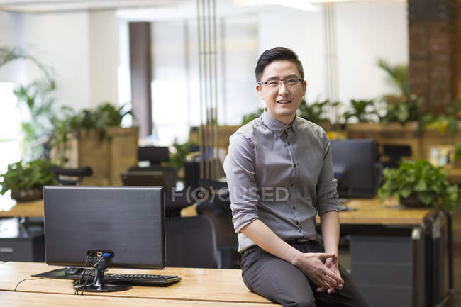 Chinese male IT worker sitting on desk at workplace — Stock Photo