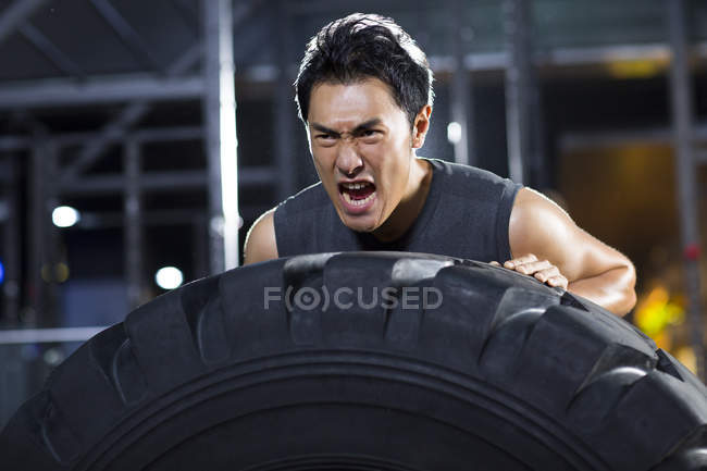 Uomo cinese spingendo grande pneumatico in palestra crossfit — Foto stock