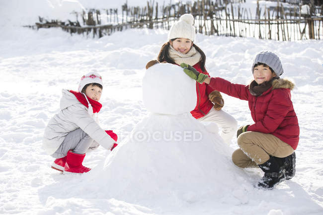 Chinese children making snowman outdoors — Stock Photo