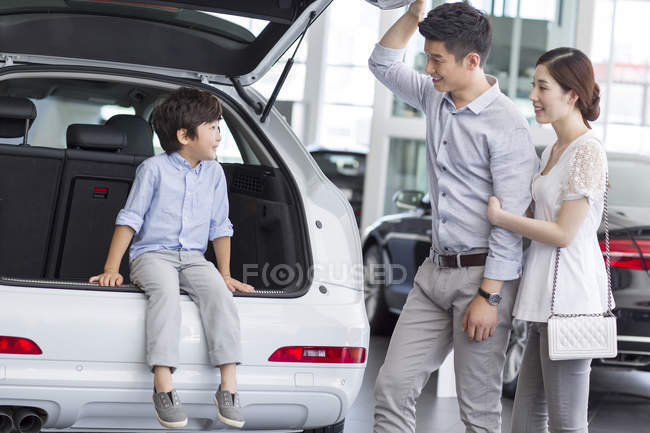 Chinese boy sitting in car trunk with parents in showroom — Stock Photo