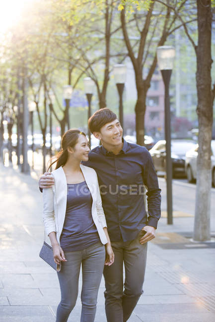 Chinese couple walking on sidewalk in town and looking away — Stock Photo