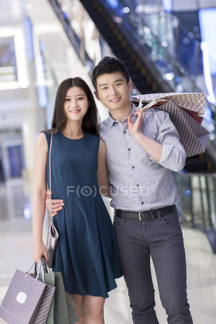 Casal chinês de pé com sacos de compras no shopping — Fotografia de Stock