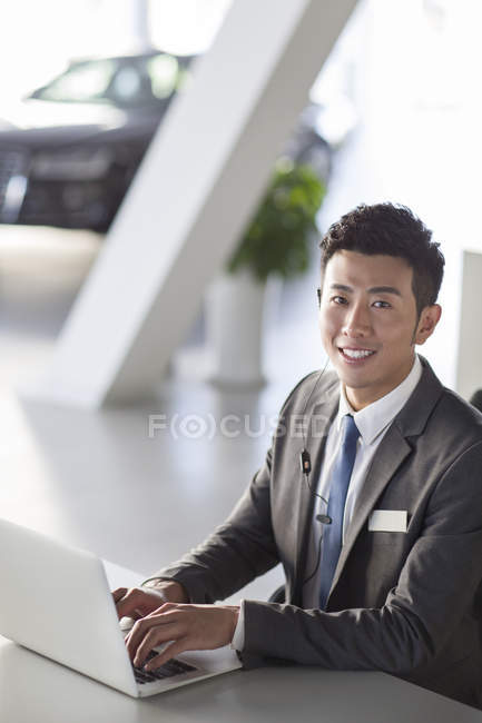 Chinese car salesman sitting with laptop — Stock Photo