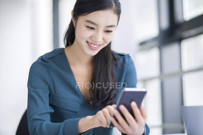 Donna d'affari cinese utilizzando smartphone in ufficio — Foto stock