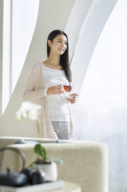 Mujer china sosteniendo taza de té negro en el interior del hogar - foto de stock