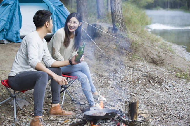Couple chinois assis à côté du feu de camp avec de la bière — Photo de stock