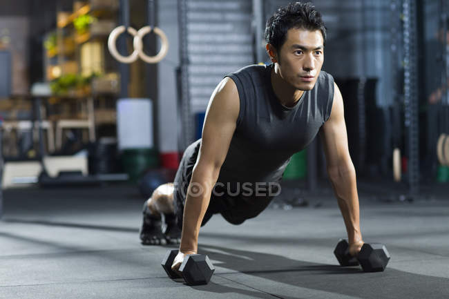 Chinese man doing push ups with dumbbells — Stock Photo