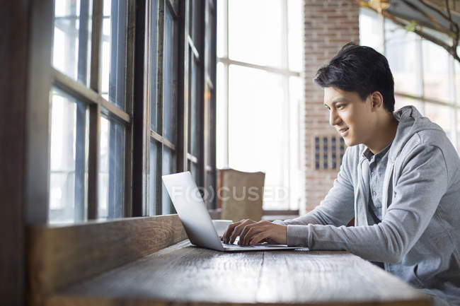 Chinese man using laptop in coffee shop — Stock Photo