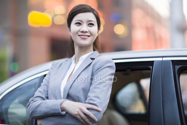 Китайська жінка, спираючись на автомобіль і посміхається — стокове фото