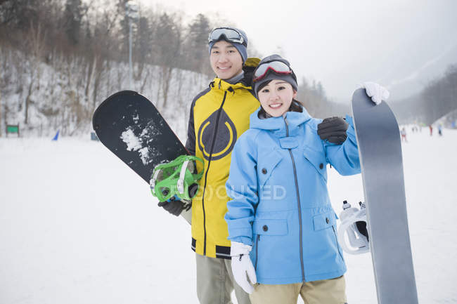 Casal chinês de snowboarders em pé na encosta — Fotografia de Stock