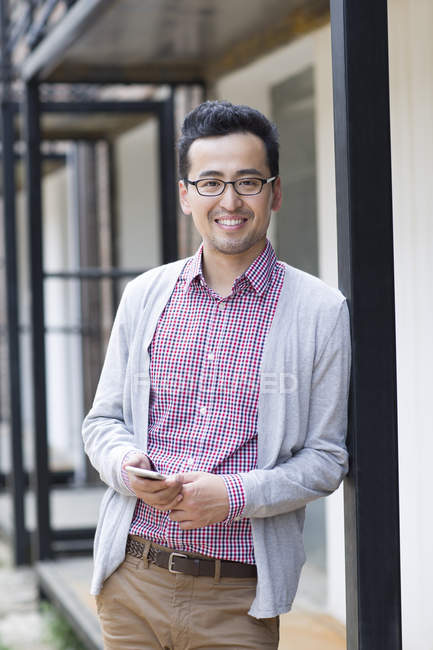 Chinese man holding smartphone and leaning on wall — Stock Photo