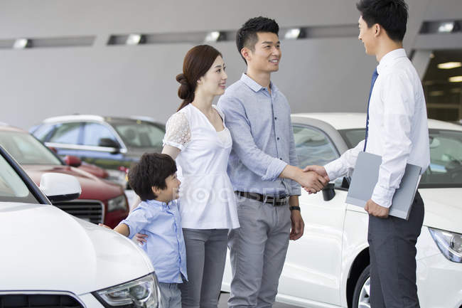 Chinese family shaking hands with car seller in showroom — Stock Photo