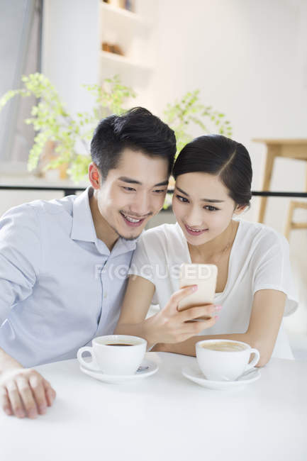 Chinese couple using smartphone in coffee shop — Stock Photo