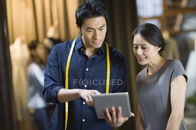 Diseñador de moda chino y cliente mirando tableta digital en la tienda - foto de stock