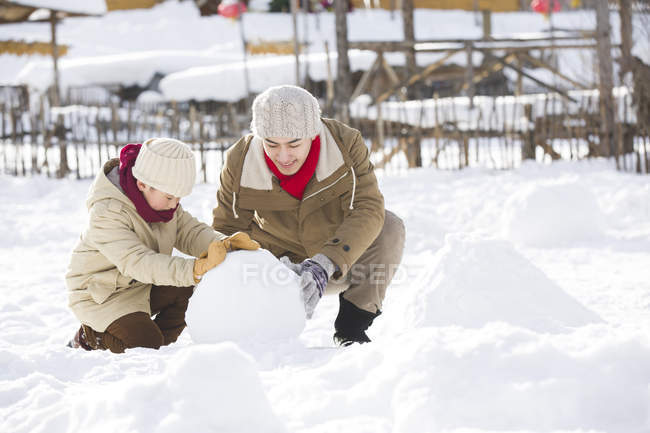 Chinese father and son rolling snowball together — Stock Photo