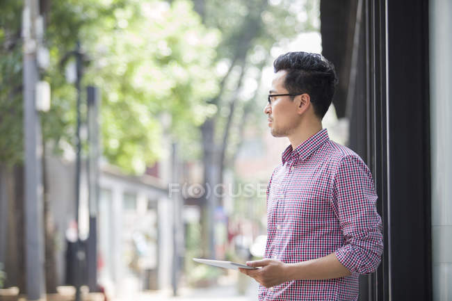 Hombre chino sosteniendo la tableta digital y mirando hacia otro lado - foto de stock