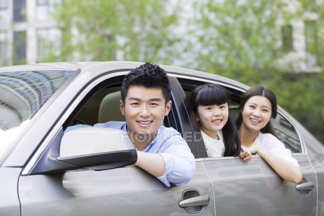 Familia china que monta y se inclina fuera del coche - foto de stock