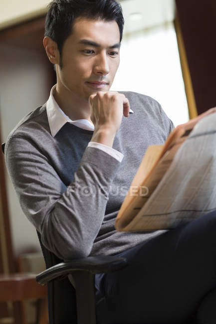 Pensivo chinês homem ler jornal em casa interior — Fotografia de Stock