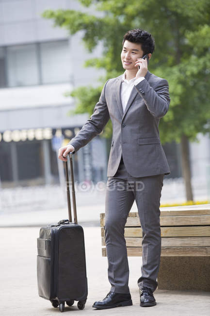 Китайский бизнесмен разговаривает по телефону с чемоданом — стоковое фото