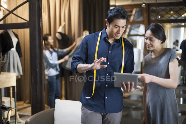 Chinese fashion designer and customer looking at digital tablet — Stock Photo