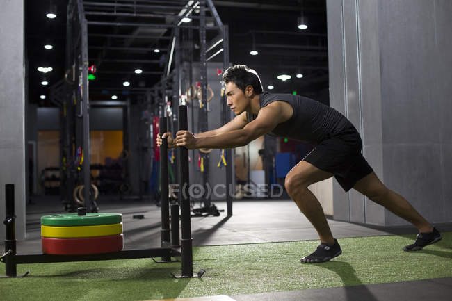 Молодой китаец толкает сани в спортзале — стоковое фото