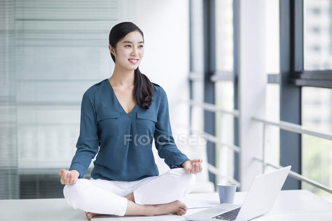 Chinese woman practicing yoga on office table — Stock Photo