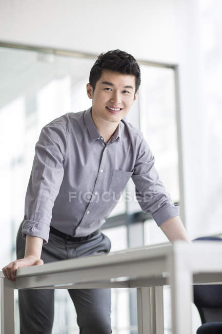 Hombre de negocios chino apoyado en la mesa y sonriendo - foto de stock