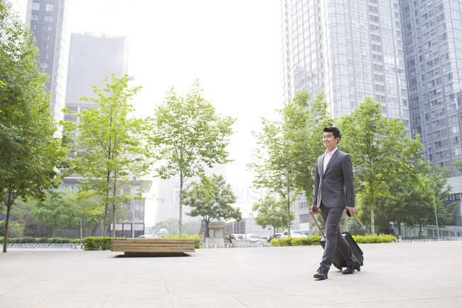 Chinese businessman walking and pulling suitcase on street — Stock Photo