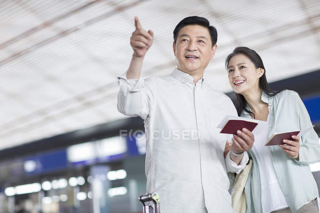 Mature chinese couple standing at airport with tickets — Stock Photo
