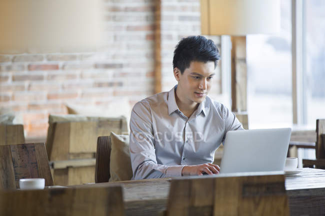 Chinese man using laptop in cafe — Stock Photo