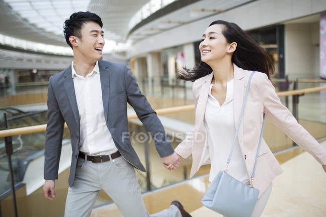 Chinese couple holding hands and running in shopping mall — Stock Photo
