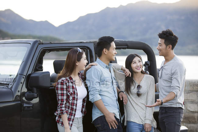 Amigos chinos charlando delante del coche en los suburbios - foto de stock