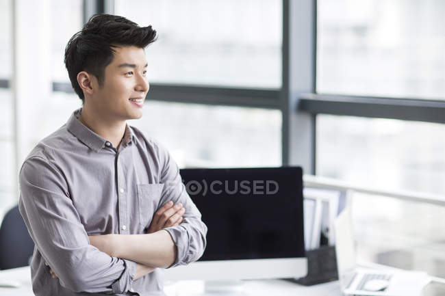 Chinese businessman looking through window in office — Stock Photo