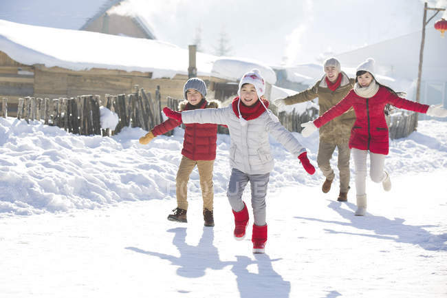 Familia china corriendo en la nieve con los brazos extendidos - foto de stock