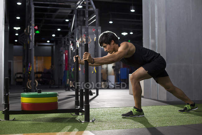 Chinese man pushing weight sled at gym — Stock Photo