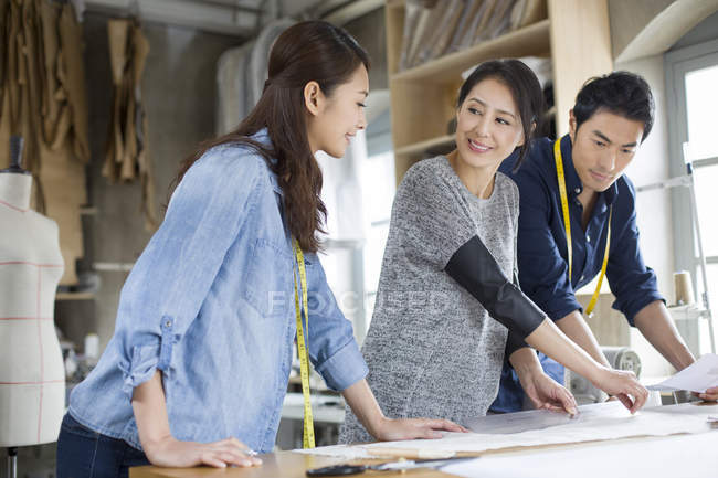 Chinese fashion designers talking and working at table in studio — Stock Photo