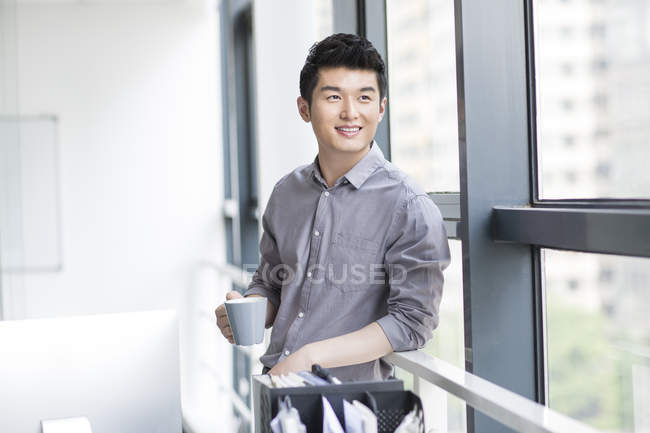 Homem de negócios chinês segurando xícara de café no escritório — Fotografia de Stock