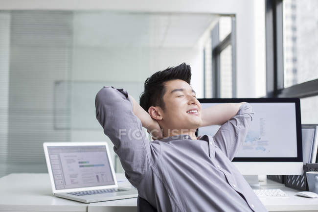 Hombre de negocios chino descansando con las manos detrás de la cabeza - foto de stock