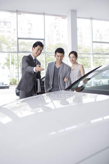 Casal chinês escolhendo carro com revendedor no showroom — Fotografia de Stock