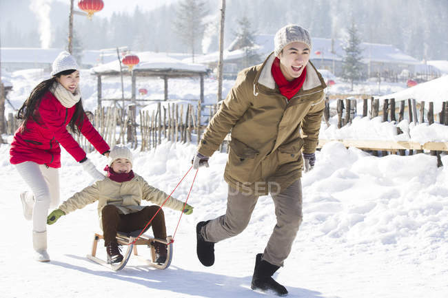 Parents chinois tirant son fils sur traîneau dans la neige — Photo de stock