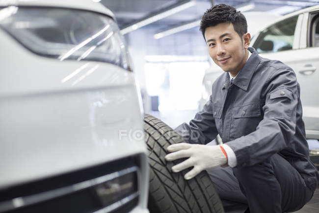 Mecánico auto chino que sostiene la rueda del coche en taller - foto de stock