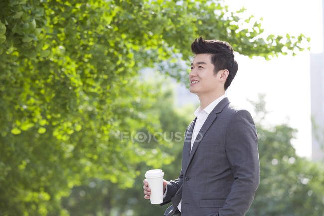 Chinese businessman holding coffee cup on street — Stock Photo