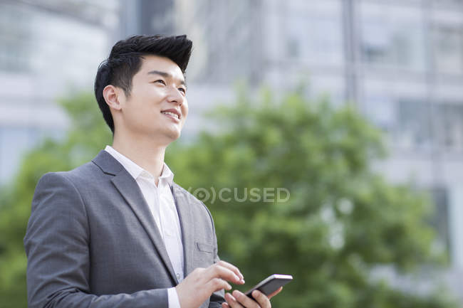 Китайський бізнесмен, стоячи з смартфон — стокове фото
