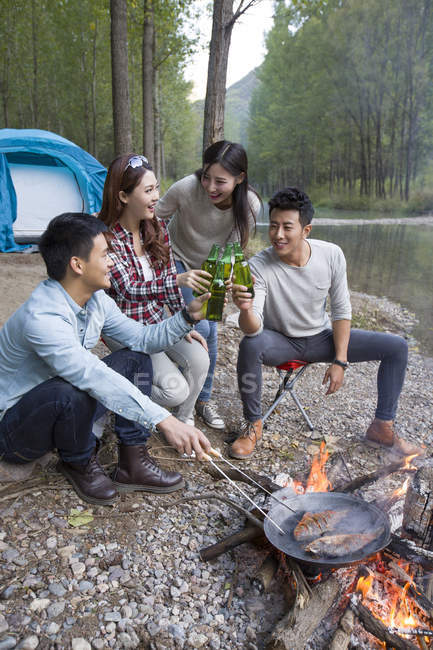 Chinese friends sitting around campfire and drinking beer — Stock Photo