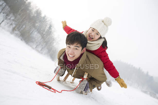 Chinese father and daughter sliding on sled together — Stock Photo