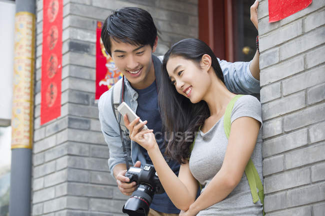 Chinese couple holding smartphone and digital camera on street — Stock Photo