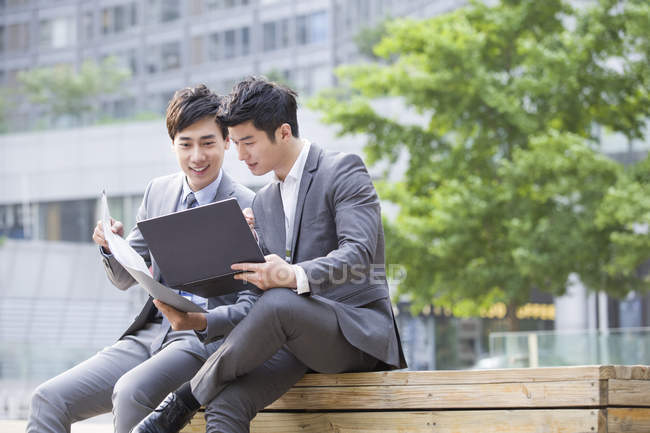 Китайские коллеги, работающие с ноутбуком на улице — стоковое фото