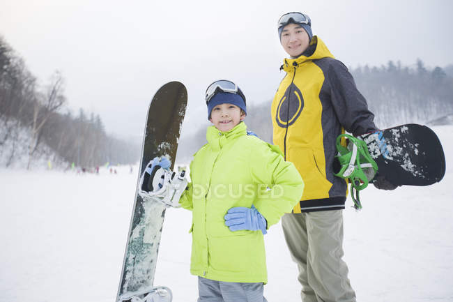 Chinese father and son standing with snowboards on slope — Stock Photo